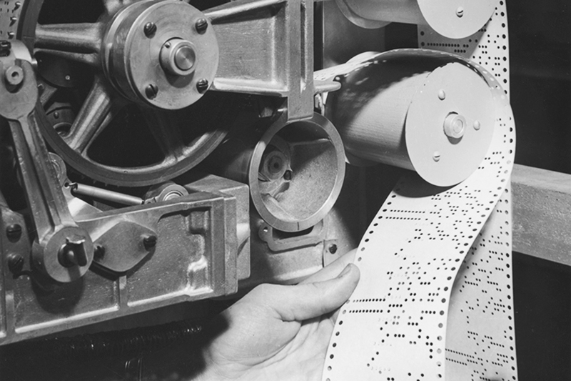 To operate the Mark I, a user had to write a program in code that could be read by the computer. That code was then converted into a series of holes punched into a paper tape, each line of holes representing a single instruction. Inside the tape reader, a series of feelers would search for holes, closing a relay switch every time one was found. Those relay switches routed information to other parts of the machine. --Courtesy of the Harvard University Archives (UAV 362.7295.8p, Box 3).