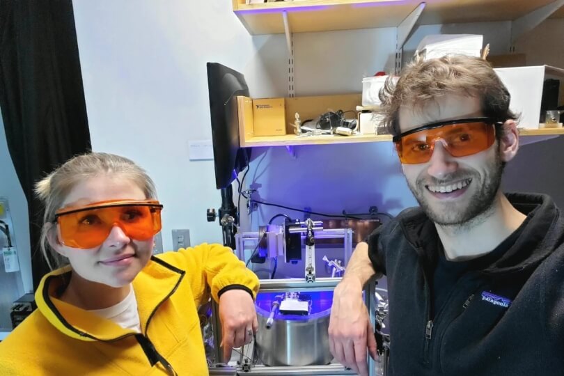 Two SEAS graduate students, one male and one female, wearing safety goggles in front of engineering equipment