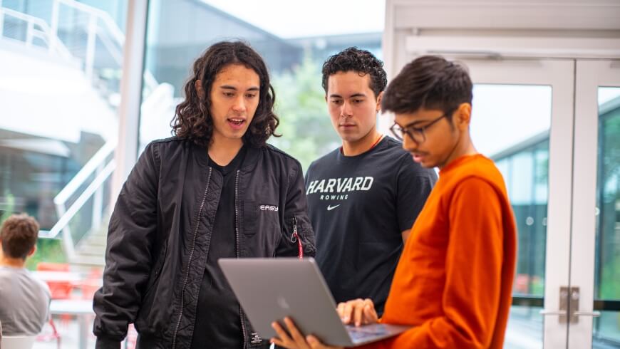 Three students hover around a laptop at the EasyA  x Harvard Hackathon at the Science and Engineering Complex