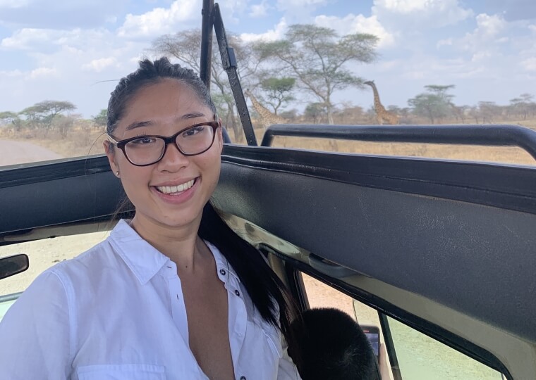Michelle Doan, A.B. ‘25 on a safari with a giraffe eating from a tree behind her