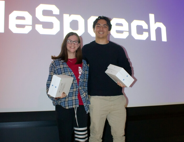 Colorado College students Kylie Bogar and Ronan Takizawa holding boxes in front of a screen displaying their product name at HackHarvard 2023