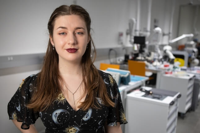 Harvard SEAS senior Molly Boswroth wearing a black shirt with moons, suns and stars, in front of electrical engineering equipment