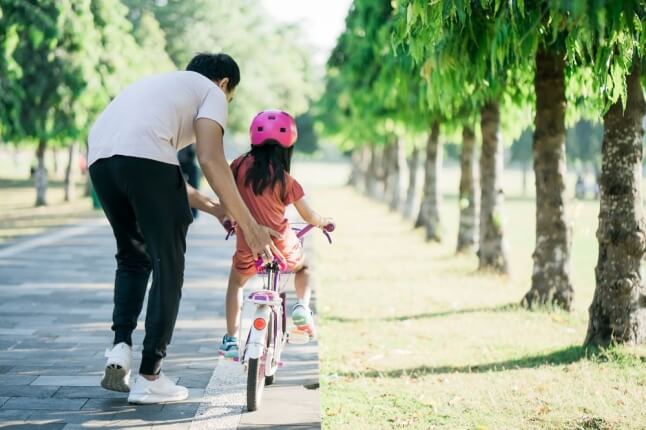 adult pushing child on bike outside