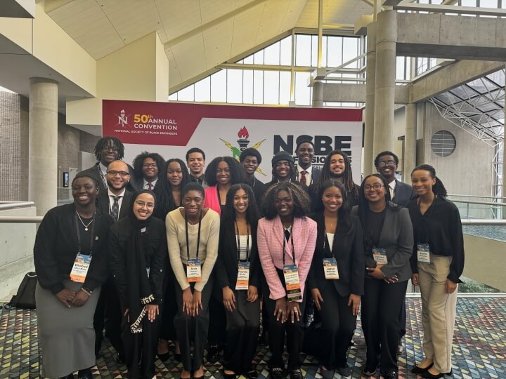 A large group of Harvard students in front of a sign for the National Society of Black Engineers national convention